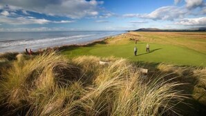 Un campo de golf frente al mar, con dunas cubiertas de hierba y cielo despejado.