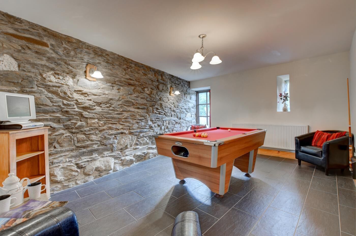A room with a pool table, stone wall, and a television on a wooden stand.