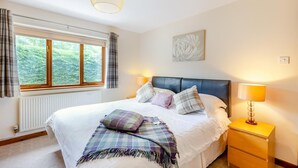Een slaapkamer met een bed, een raam met gordijnen, een radiator, een nachtkastje met een lamp en een aan de muur hangend kunstwerk.