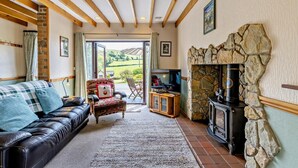 A cozy living room with a leather sofa, a patterned armchair, a television, and a stone fireplace. - 2 Bed in Aberystwyth (oc-99869) (Pontarfynach)