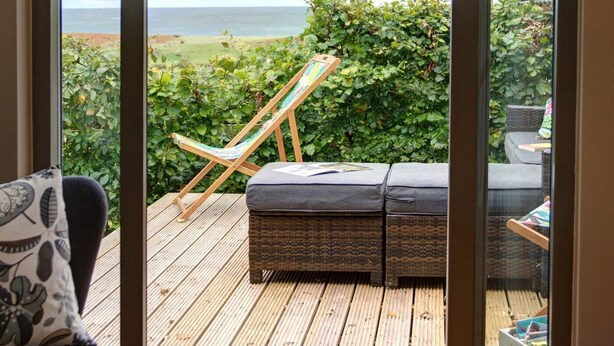Een kamer met een schuifdeur naar een terras buiten, met een zithoek met kussens en een loungestoel.