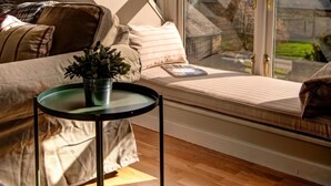 Een gezellige kamer met een schuine kap, een vensterbank met kussens, een kleine tafel met een plant en uitzicht op het exterieur.