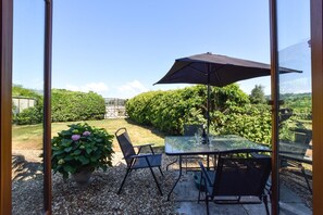 Un patio con mesa y sillas de vidrio, una sombrilla y una planta en maceta.