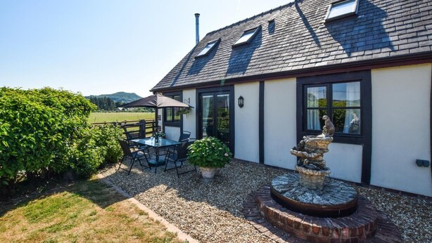 Ein Haus mit Terrasse, Tisch, Stühlen, einer Fontäne und Blick auf die Landschaft.