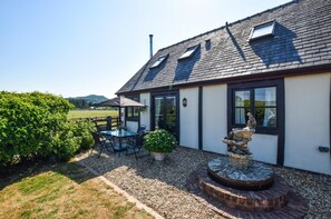 Ein Haus mit Terrasse, Tisch, Stühlen, einer Fontäne und Blick auf die Landschaft.