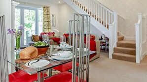 A dining area with a glass table, red chairs, and a bowl of salad. There is a staircase with white railings leading to an upper level. - 1 Bed in Embleton (oc-566732) (Embleton)