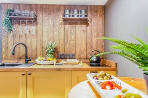 Cozinha com armários de madeira, chaleira preta, tigela de frutas e tábua de corte.
