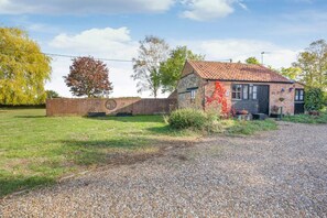 A rustic building with a gravel driveway, a brick wall, and a tree with autumn leaves. - 1 Bed in Yaxham (oc-w33631) (Mattishall)