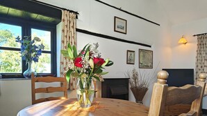 Una mesa de comedor de madera con sillas, un florero y una chimenea al fondo.