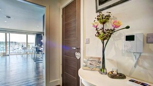 Een hotel receptie met een houten deur, een welkomstbord, een bloevas, een telefoon en uitzicht op de stad door grote ramen.