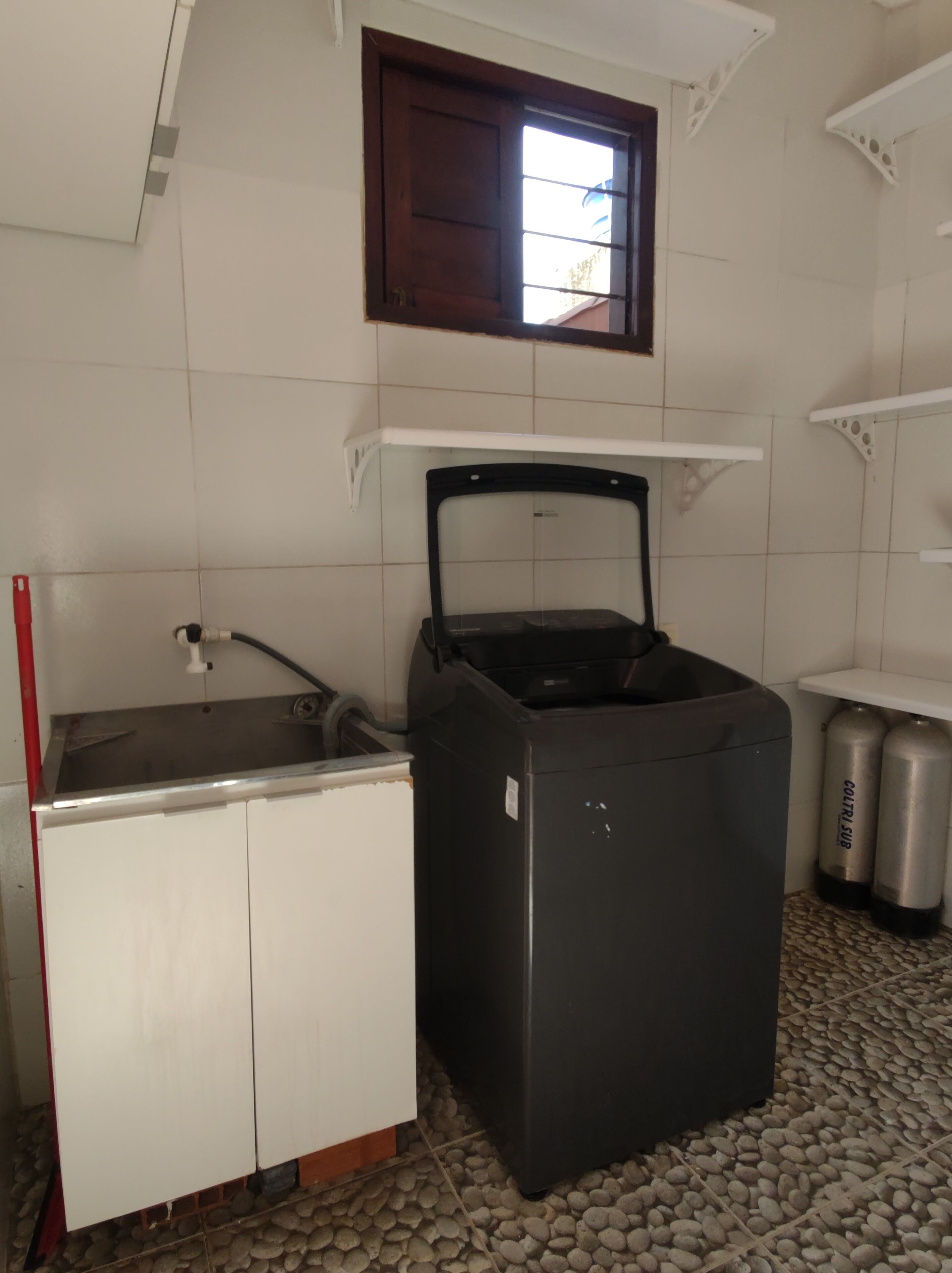 A compact kitchen with a sink, a black refrigerator, and two gas cylinders.