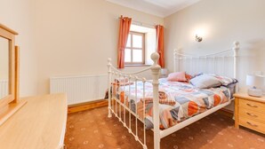 Quarto com cama, mesa de cabeceira, cômoda, janela com cortinas e radiador.