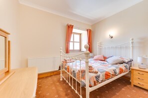 A bedroom with a bed, a nightstand, a dresser, a window with curtains, and a radiator.