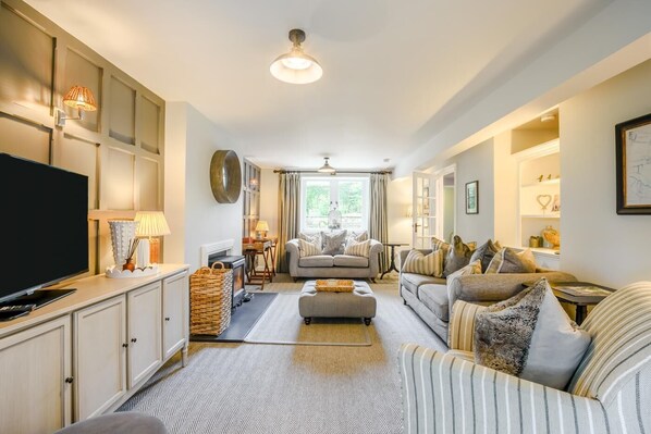 A spacious living room with a television, sofas, a fireplace, and a ceiling fan.