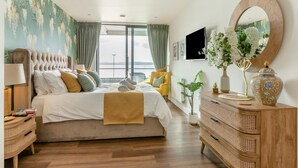 A bedroom with a large bed, a wooden dresser, a mirror, and a view of the outdoors. - 2 Bed in Torquay (oc-o33463) (Torquay)
