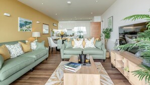A modern living room with two green sofas, a coffee table, and a dining area in the background. - 2 Bed in Torquay (oc-o33463) (Torquay)