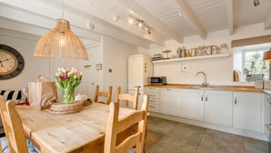 Une cuisine moderne avec des meubles blancs, une table à manger en bois et un luminaire suspendu.