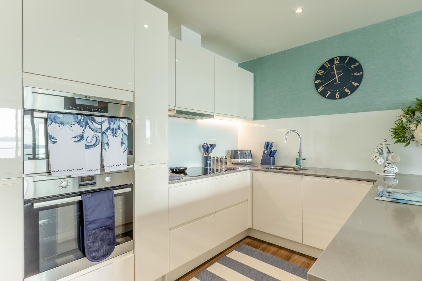 A modern kitchen with white cabinetry, a stainless steel oven, a microwave, and a blue clock on the wall.