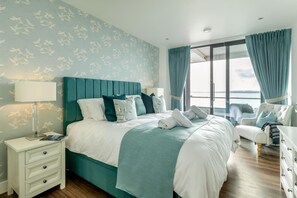 A modern hotel room with a large bed, a nightstand, a dresser, and a view of the sea through the window. - 2 Bed in Torquay (oc-a33462) (Torquay)