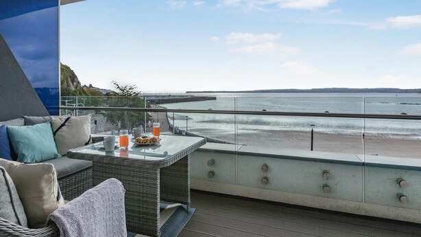 Ein Balkon mit einem Glastisch, Sitzgelegenheiten und Blick aufs Meer.