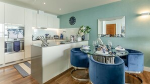 Eine moderne Küche mit weißen Schränken, einer zentralen Kochinsel und einem Essbereich mit blauen Stühlen und einem Glastisch.