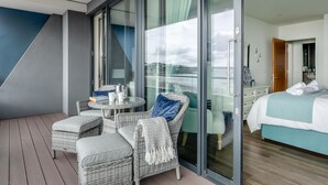 Ein Balkon mit Korbmöbeln, einem kleinen Tisch und einem Bett im angrenzenden Zimmer.