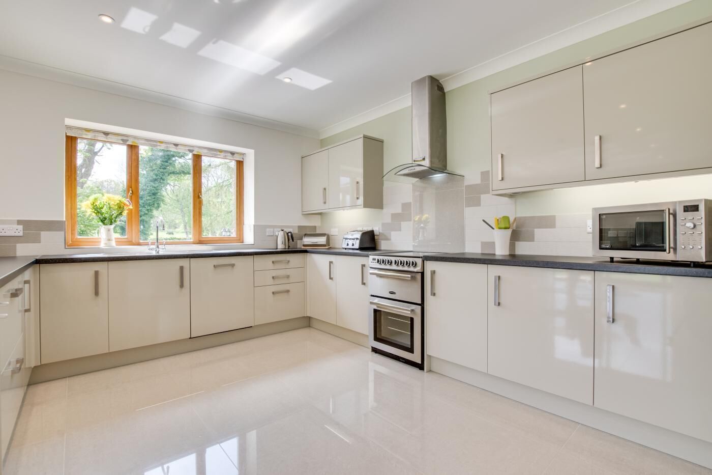 Une cuisine moderne avec des meubles blancs, une cuisinière en acier inoxydable, un four à micro-ondes et une fenêtre donnant sur un paysage verdoyant.