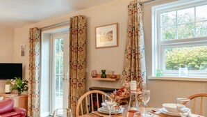Un comedor con una mesa preparada para cuatro, un televisor y una ventana con cortinas.
