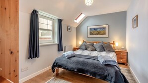 Un dormitorio con una cama, una mesita de noche, una ventana con cortinas, una lámpara en el techo y un cuadro en la pared.