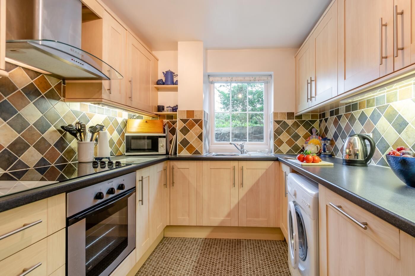 A modern kitchen with wooden cabinets, a microwave, a stove, and a washing machine.