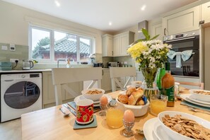 Une cuisine moderne équipée d’un lave-linge intégré, d’une table à manger dressée pour le petit-déjeuner et offrant une vue sur l’extérieur grâce à de grandes fenêtres.