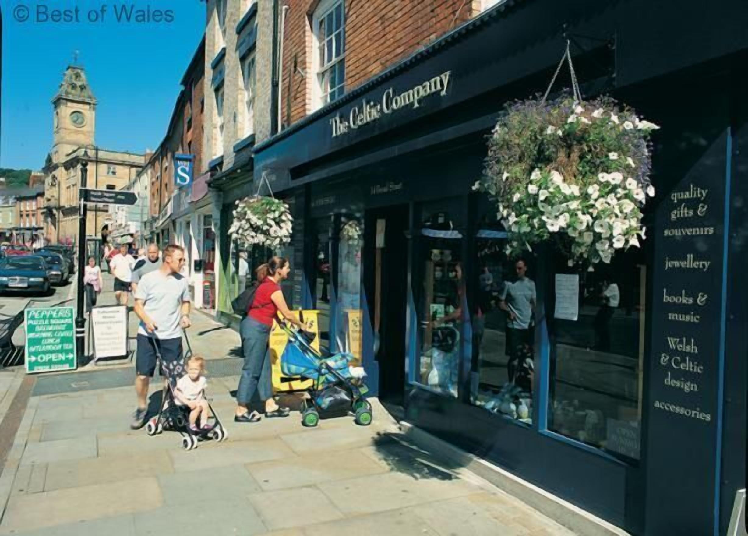 A storefront with hanging flower baskets and a sign for 'The Celtic Company' offering quality gifts, souvenirs, and Welsh & Celtic design accessories.