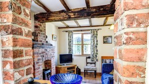 A rustic room with exposed wooden beams, a brick fireplace, a television, and a cozy seating area. - 1 Bed in Welshpool (oc-75714) (Meifod)