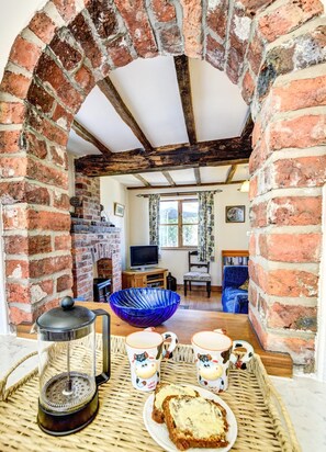 A rustic room with exposed wooden beams, a brick fireplace, a television, and a cozy seating area. - 1 Bed in Welshpool (oc-75714) (Meifod)