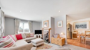 A modern living room with a sofa, ottoman, flat-screen TV, fireplace, dining area, and kitchenettes. - 3 Bed in Seahouses (oc-566761) (Seahouses)