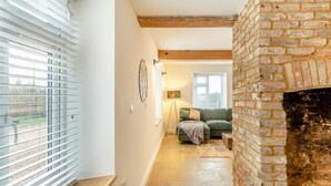 Ein Flur mit Kamin aus Ziegelsteinen, einem grünen Sofa und einem Fenster mit Jalousien.