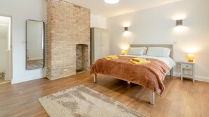Ein Schlafzimmer mit Kamin aus Ziegelsteinen, einem Bett mit brauner Decke, Nachttischlampen und einem Spiegel an der Wand.