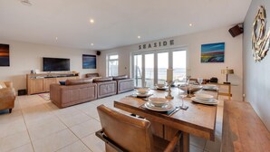 A spacious living area with a large sofa, a dining table set for four, and a television on a wooden cabinet. - 4 Bed in Beadnell (oc-566397) (Beadnell)