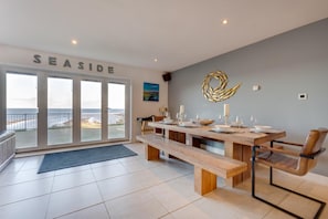 A dining area with a large table set for four, a bench, and a view of the sea through a glass door. - 4 Bed in Beadnell (oc-566397) (Beadnell)