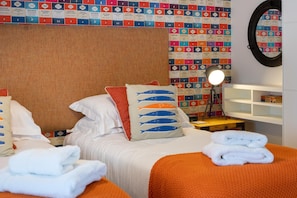 A hotel room with a bed, pillows, a nightstand, a lamp, and a wall with colorful posters. - 2 Bed in Seahouses (oc-565751) (Seahouses)