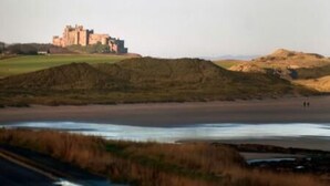 Eine Küstenlandschaft mit einem Schloss auf einem Hügel, einem Strand und dem Ozean.