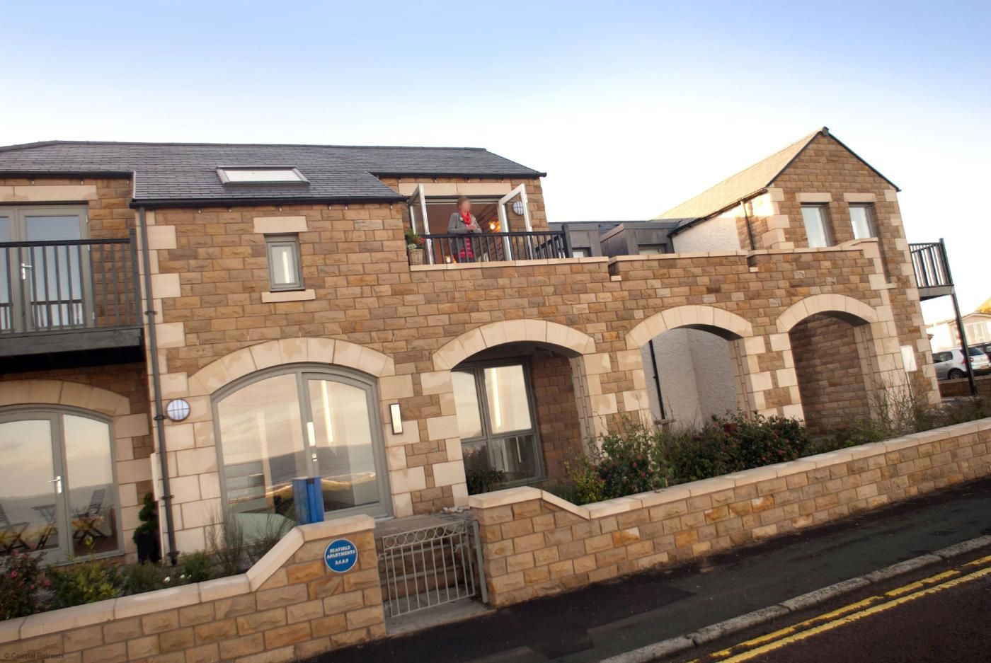 A multi-story residential building with a stone facade, large windows, and a gated entrance.