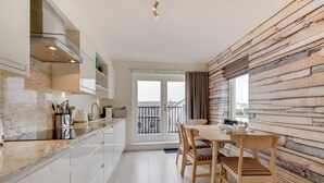 Eine moderne Küche mit Marmorarbeitsplatte, weißen Schränken und einem Essbereich mit Holztischen und einer Holztischplatte.