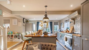 Una cocina amplia con una isla central, un comedor con una silla tapizada y vistas al exterior a través de ventanas grandes.