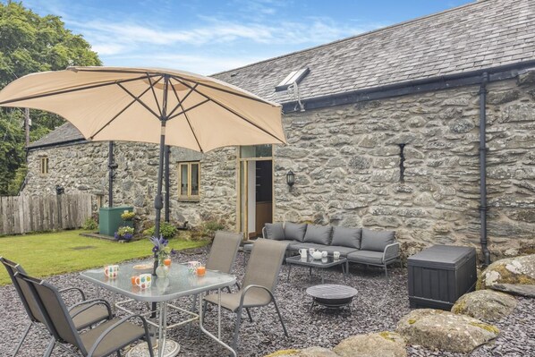 A stone building with a patio area featuring a table, chairs, a sofa, and a large umbrella.