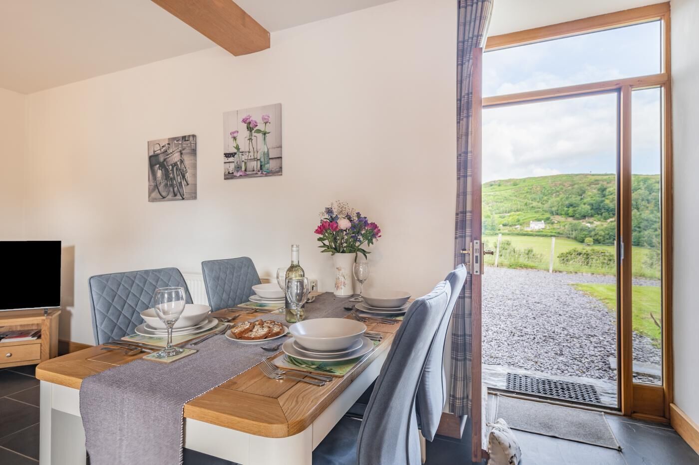 Un coin repas avec une table dressée pour quatre personnes, un téléviseur sur le côté gauche et une vue magnifique par la fenêtre.