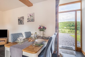 A dining area with a table set for four, a television on the left, and a scenic view through the window.