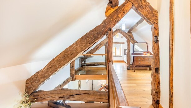 A rustic room with exposed wooden beams, a wooden staircase, and a bed with a wooden headboard.