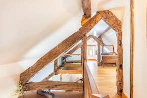 A rustic room with exposed wooden beams, a wooden staircase, and a bed with a wooden headboard.