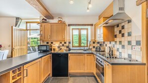 A modern kitchen with wooden cabinets, a black dishwasher, a microwave, a toaster, and a large window offering a view of greenery.